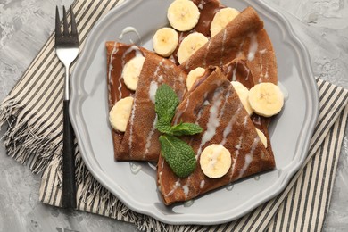 Photo of Delicious chocolate crepes with banana, condensed milk and mint served on grey table, top view