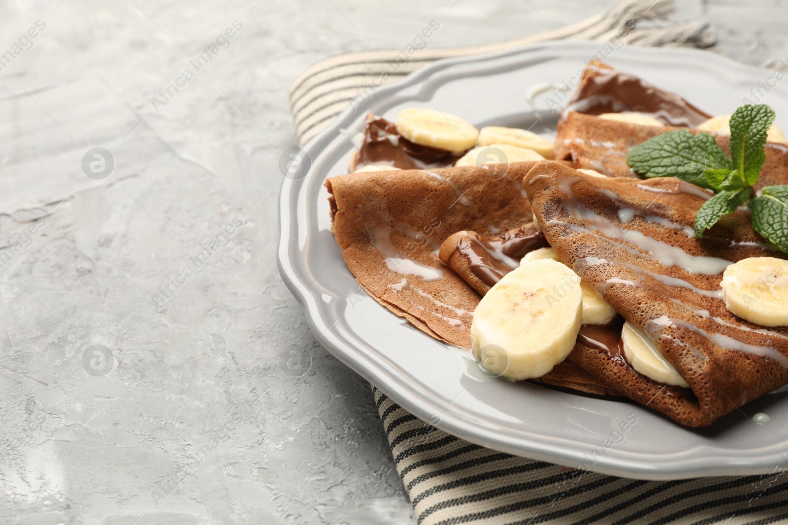 Photo of Delicious chocolate crepes with banana, condensed milk and mint served on grey table, closeup. Space for text