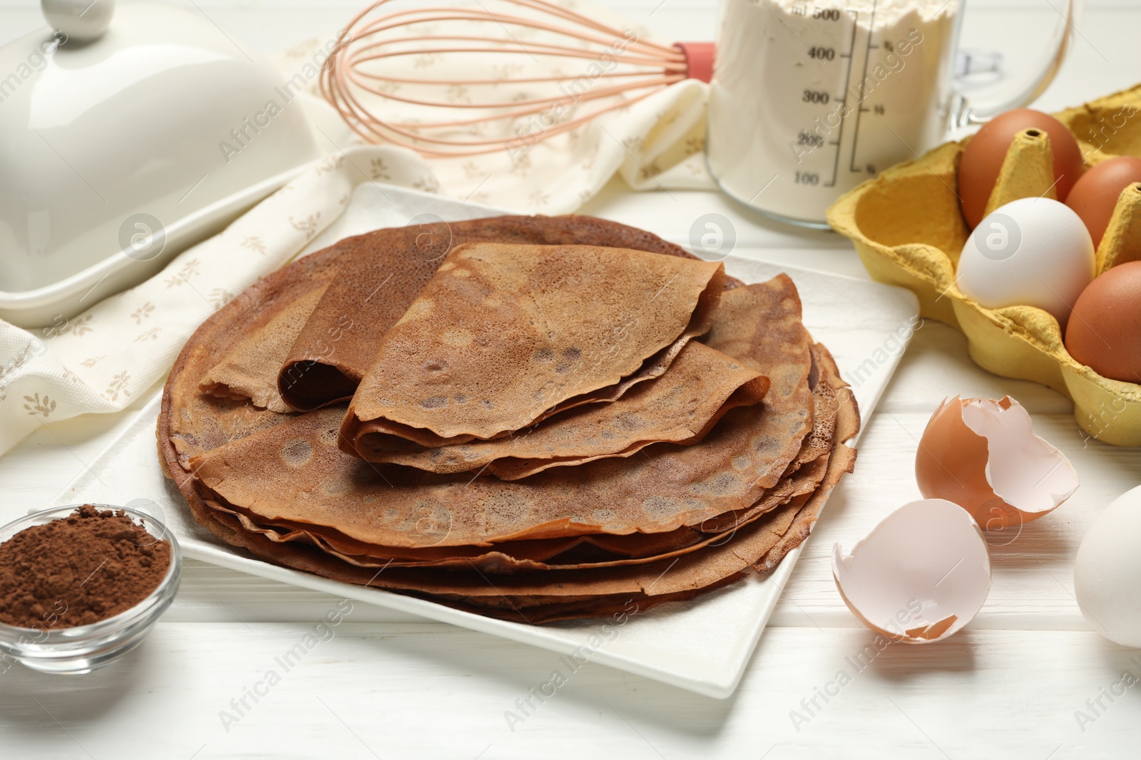 Photo of Delicious chocolate crepes and ingredients on white wooden table, closeup