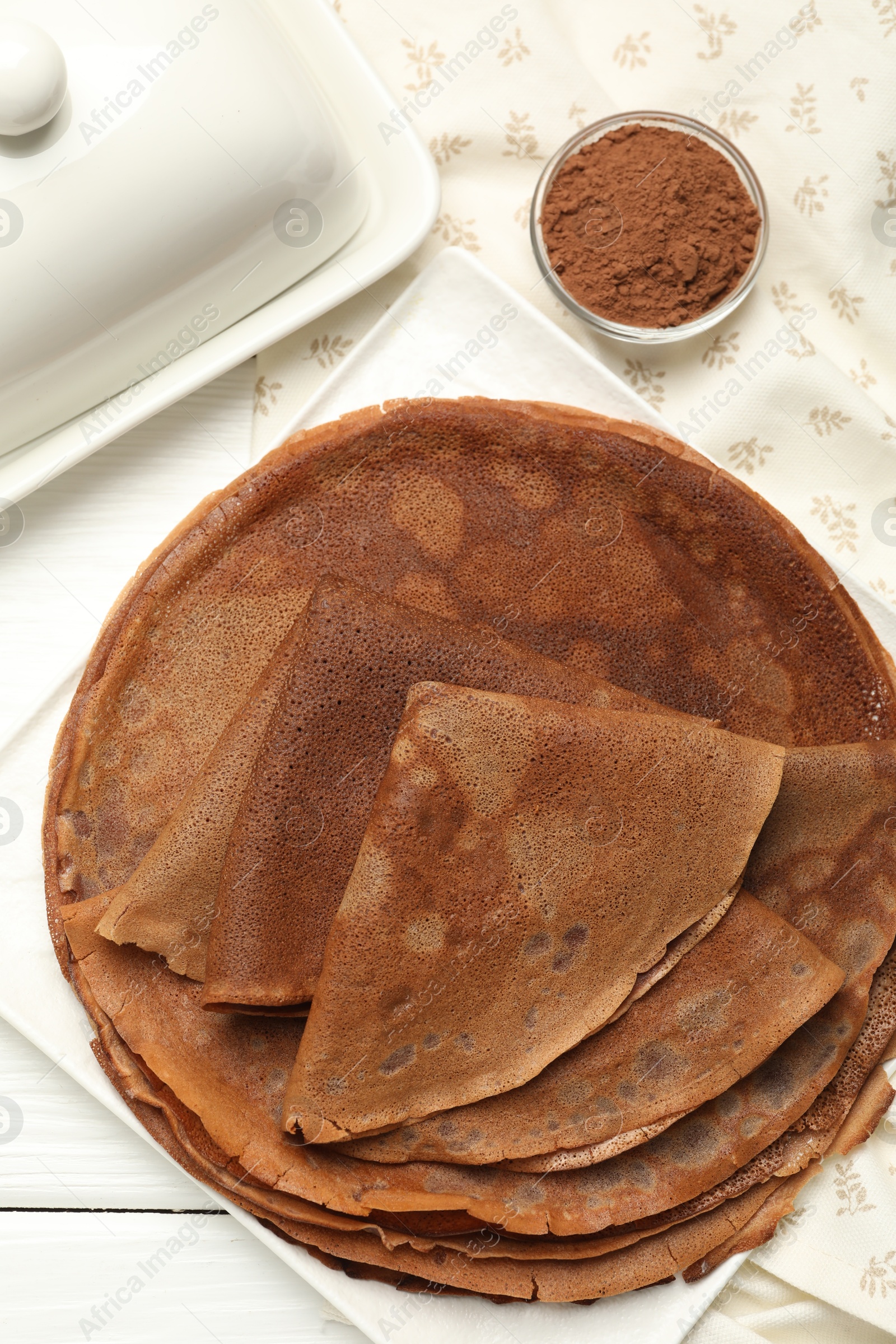 Photo of Delicious chocolate crepes and cocoa powder on white wooden table, top view