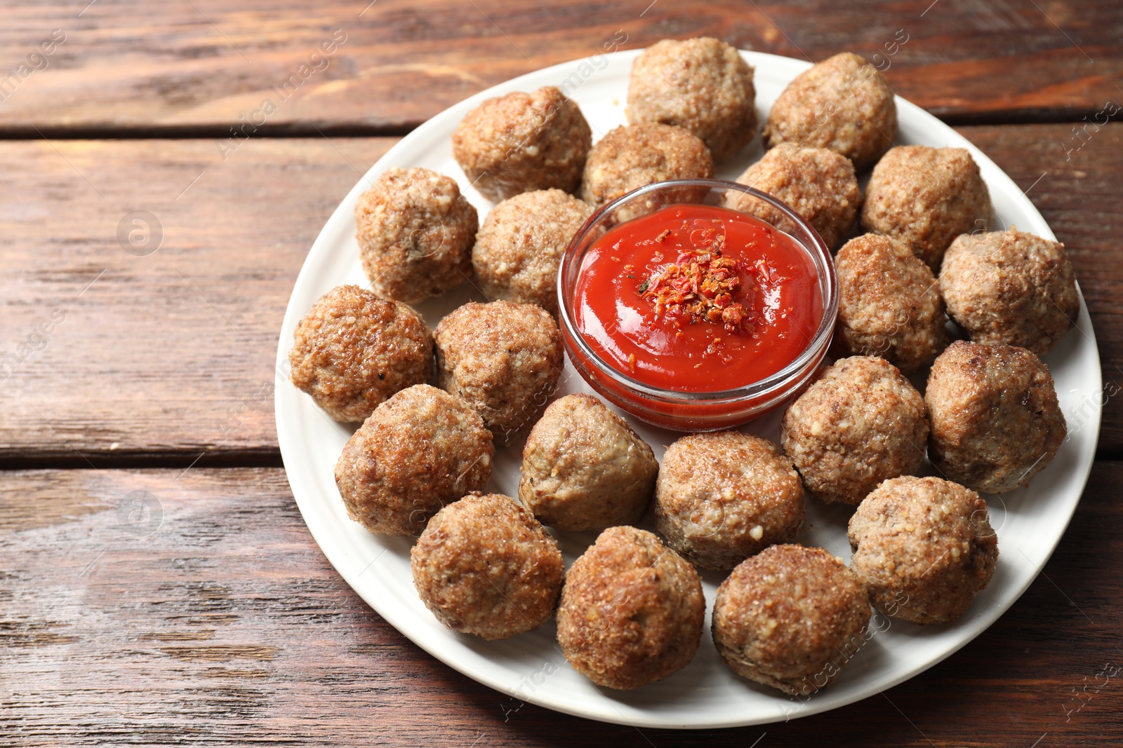 Photo of Delicious meatballs with ketchup and spices on wooden table, closeup