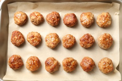 Photo of Many delicious meatballs on parchment in baking dish, top view