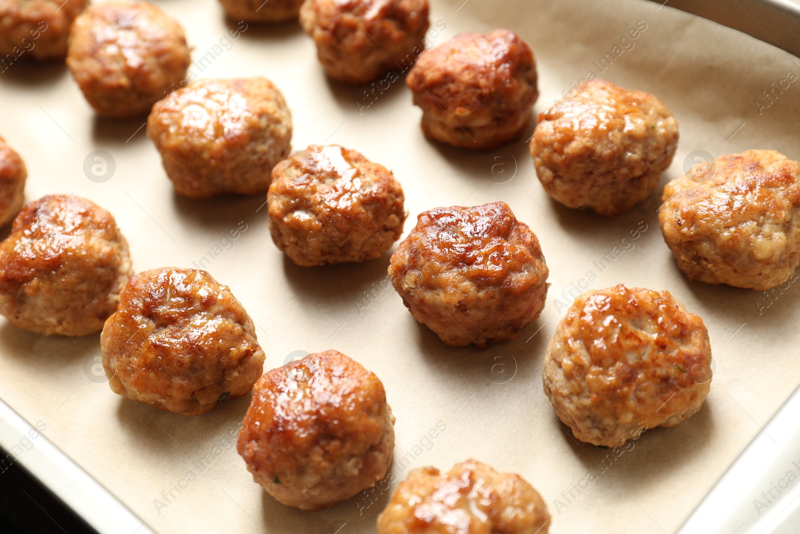 Photo of Many delicious meatballs on parchment in baking dish, closeup