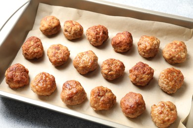 Photo of Many delicious meatballs in baking dish on grey textured table, closeup