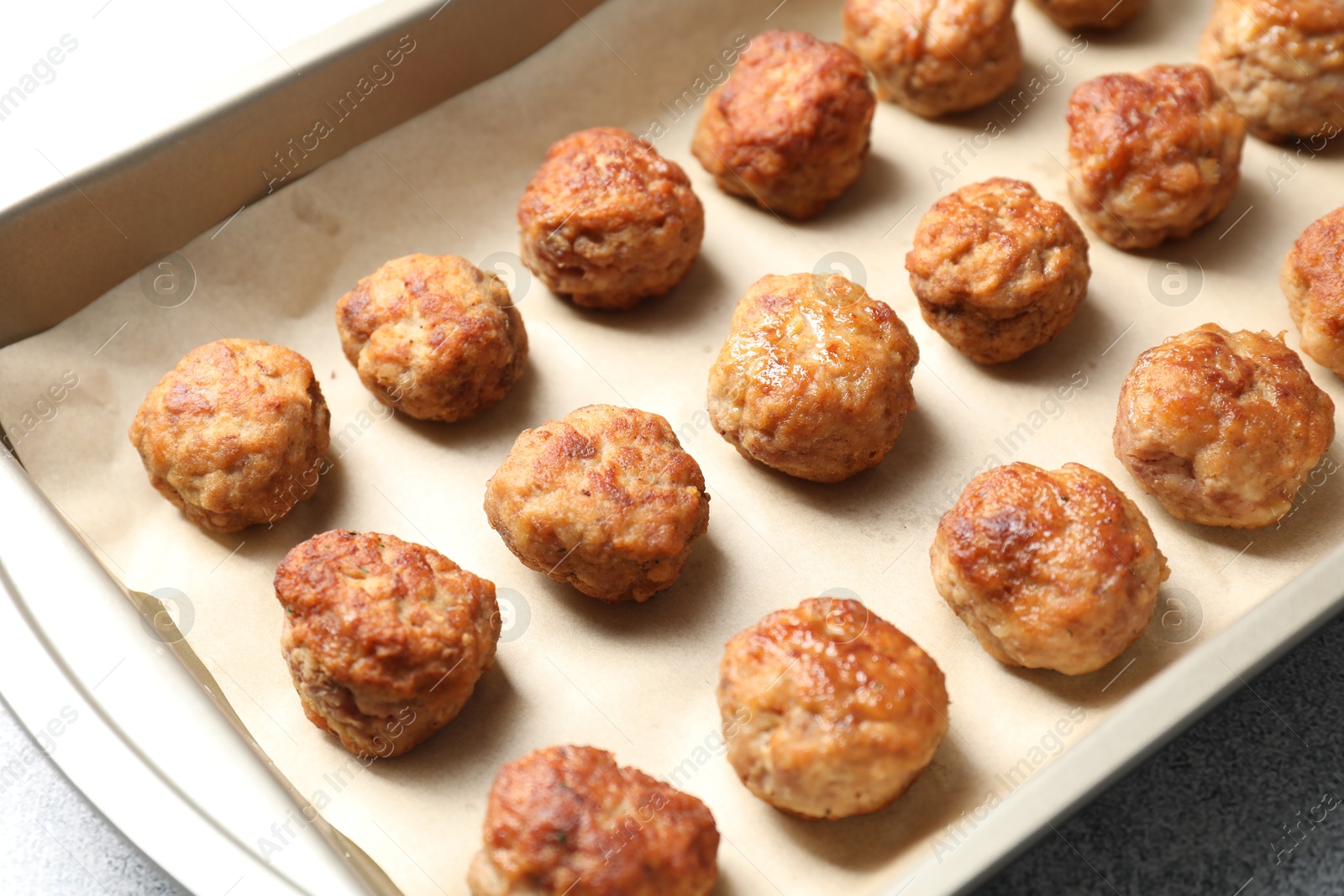 Photo of Many delicious meatballs in baking dish on grey textured table, closeup