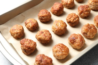 Photo of Many delicious meatballs in baking dish on grey textured table, closeup