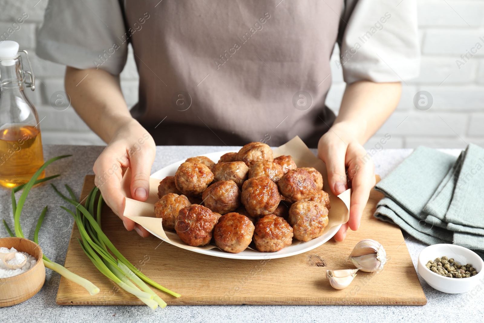 Photo of Woman holding plate with delicious meatballs at light textured table, closeup