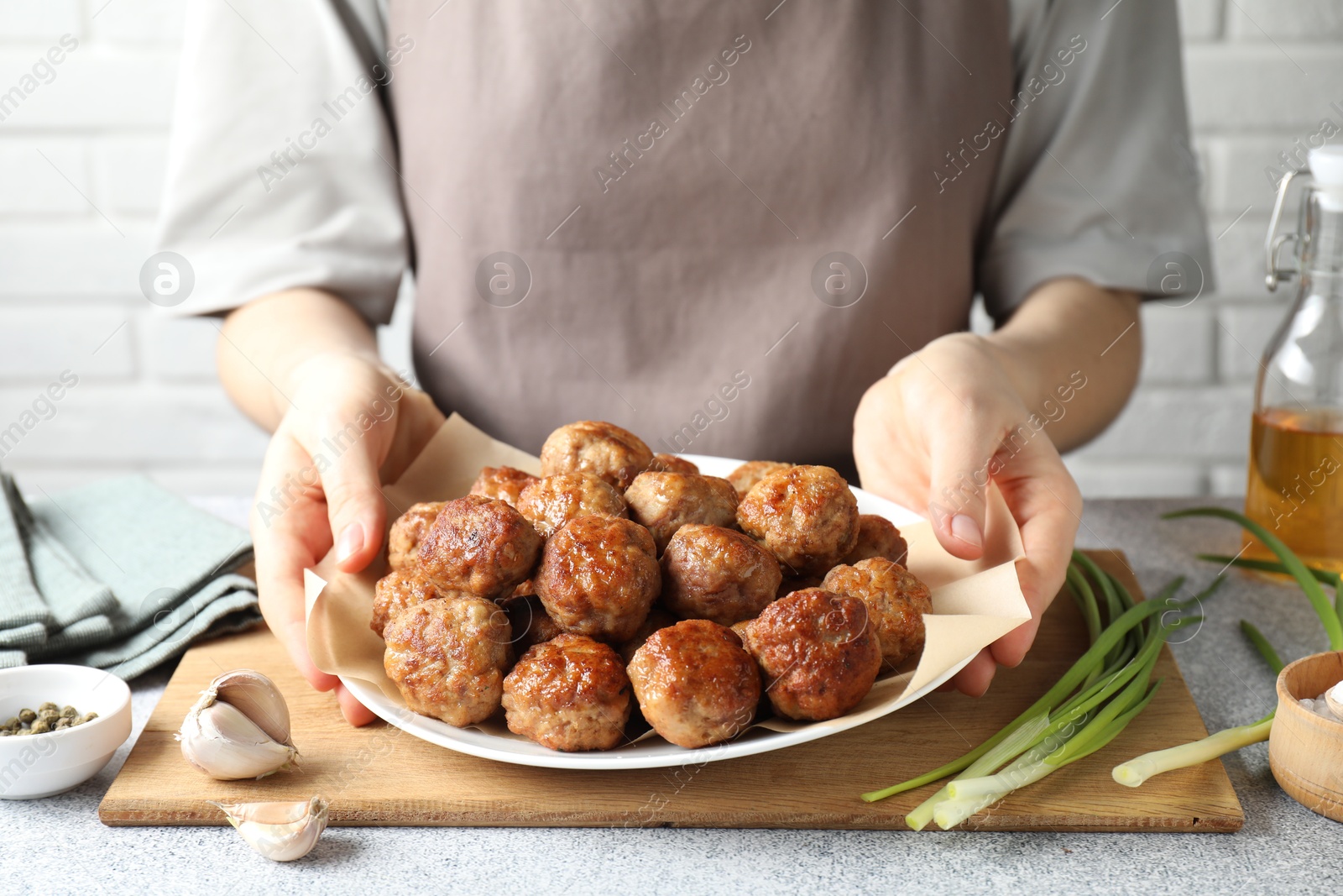 Photo of Woman holding plate with delicious meatballs at light textured table, closeup