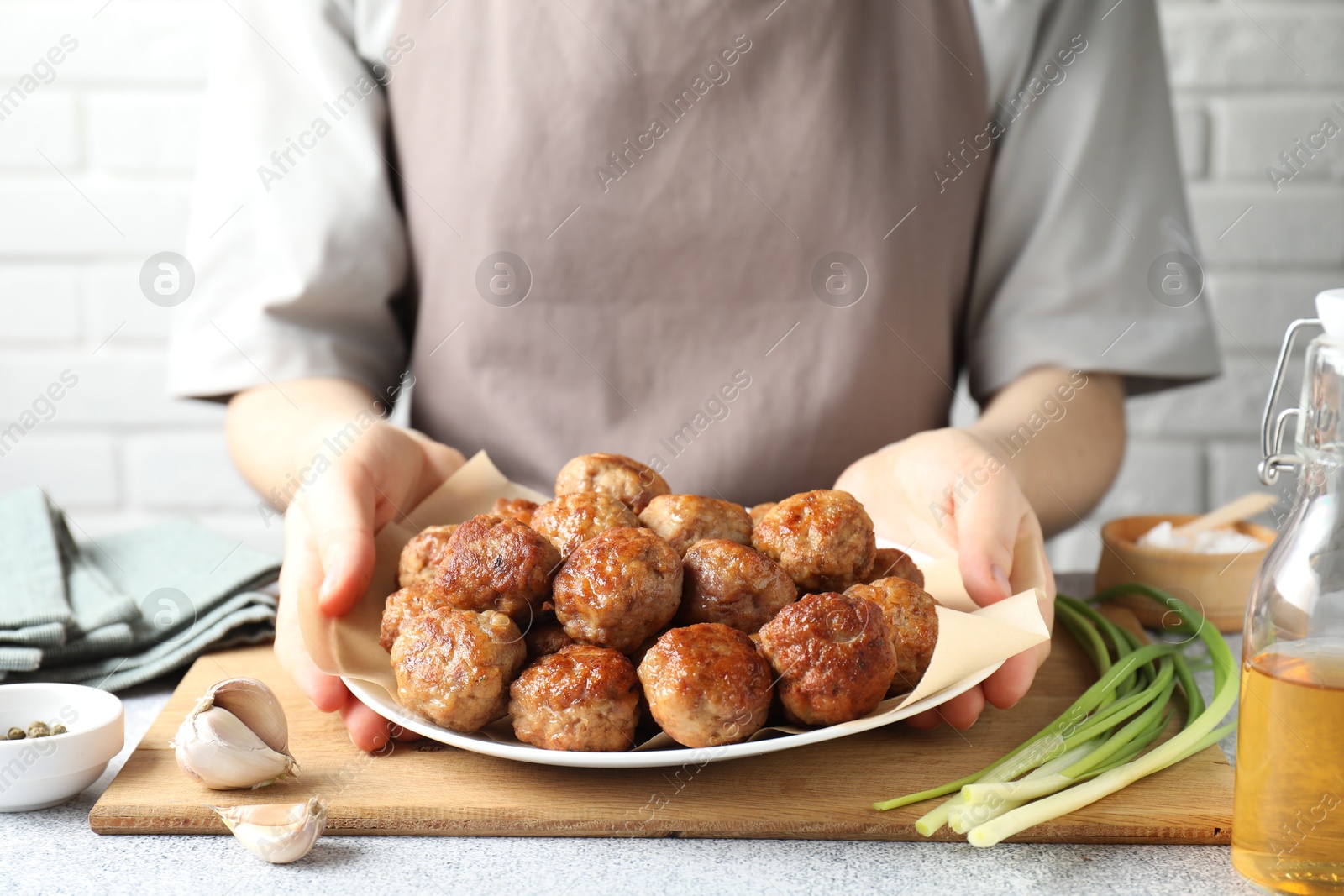 Photo of Woman holding plate with delicious meatballs at light textured table, closeup