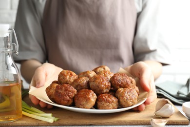 Photo of Woman holding plate with delicious meatballs at table, closeup