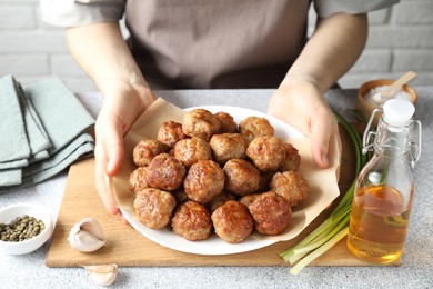 Photo of Woman holding plate with delicious meatballs at light textured table, closeup