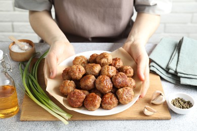 Photo of Woman holding plate with delicious meatballs at light textured table, closeup