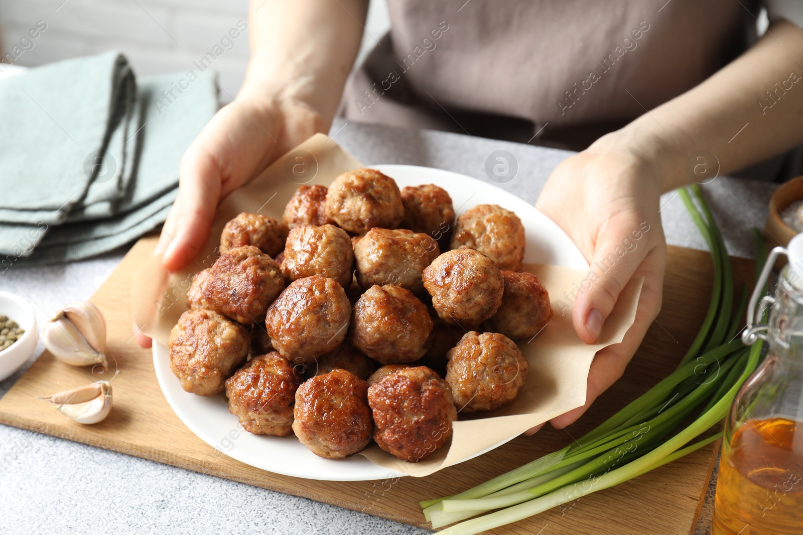 Photo of Woman holding plate with delicious meatballs at light textured table, closeup