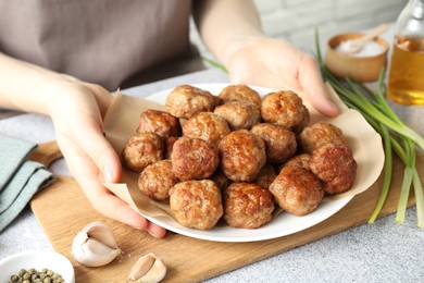 Photo of Woman holding plate with delicious meatballs at light textured table, closeup