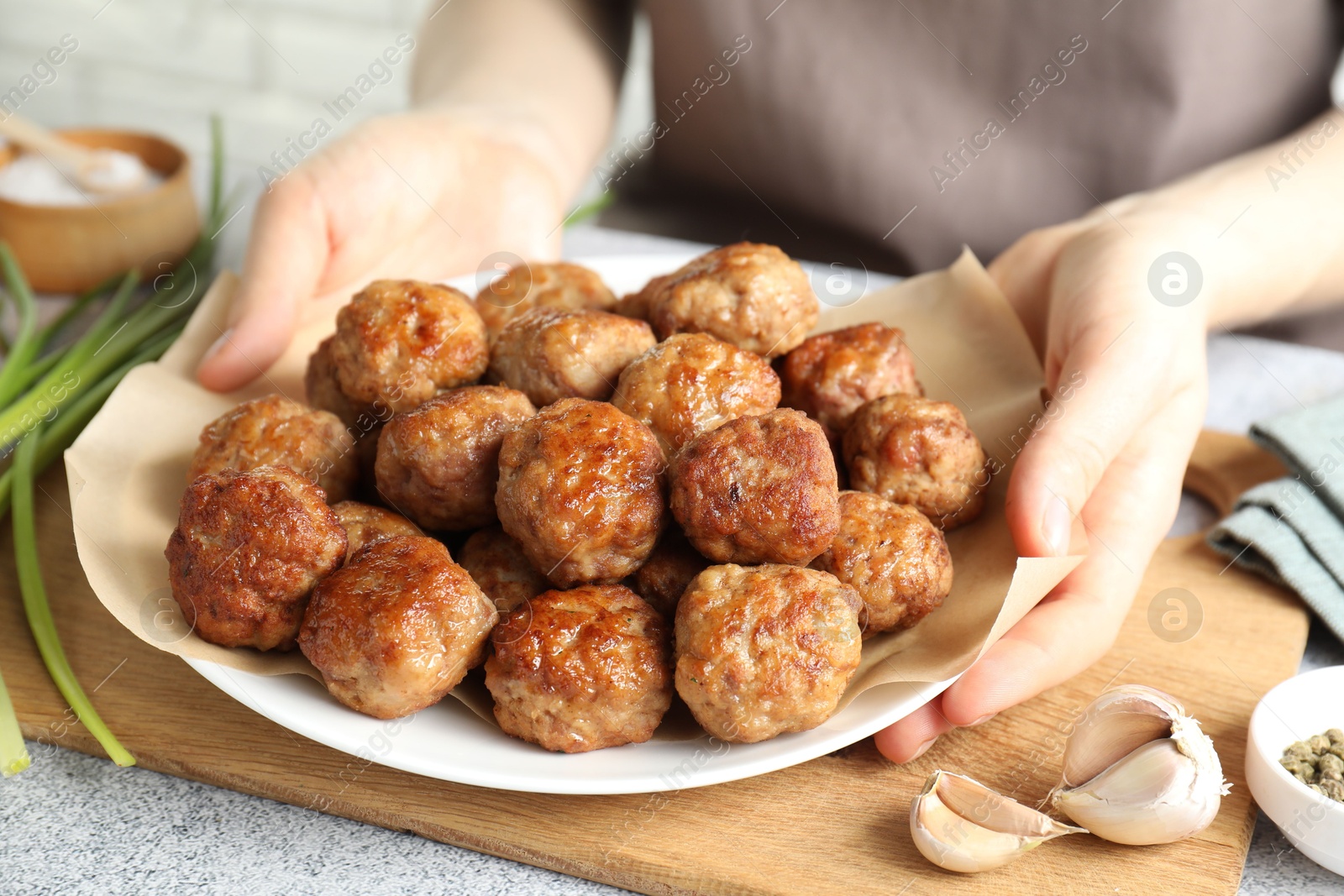 Photo of Woman holding plate with delicious meatballs at light textured table, closeup