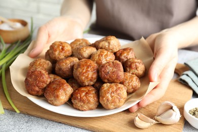 Photo of Woman holding plate with delicious meatballs at light textured table, closeup