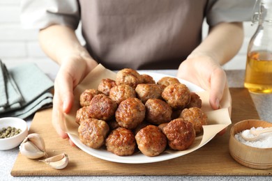 Photo of Woman holding plate with delicious meatballs at light textured table, closeup