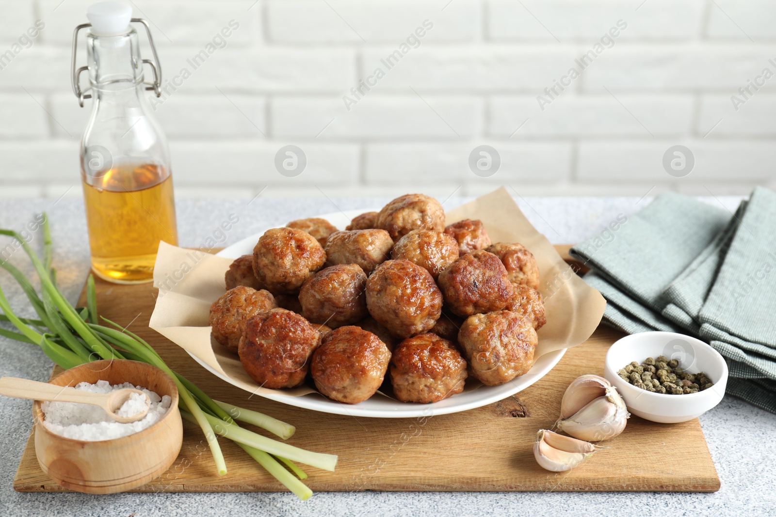 Photo of Many delicious meatballs, green onion, garlic, oil and spices on light textured table