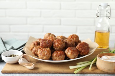 Photo of Many delicious meatballs, green onion, garlic, oil and spices on light textured table