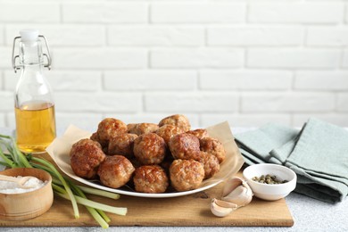 Photo of Many delicious meatballs, green onion, garlic, oil and spices on light textured table