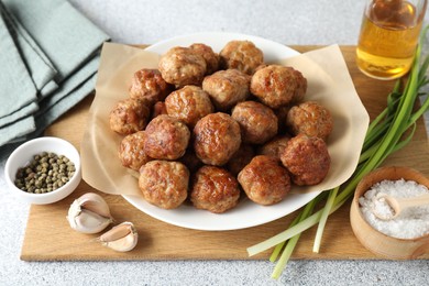 Photo of Many delicious meatballs, green onion, garlic, oil and spices on light textured table, closeup