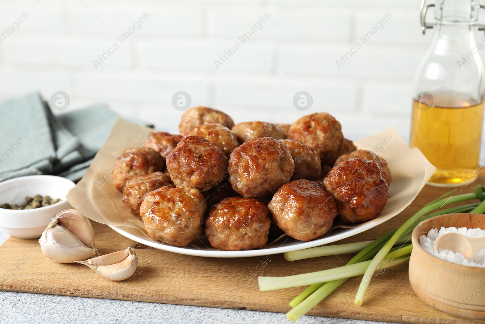 Photo of Many delicious meatballs, green onion, garlic, oil and spices on light textured table, closeup