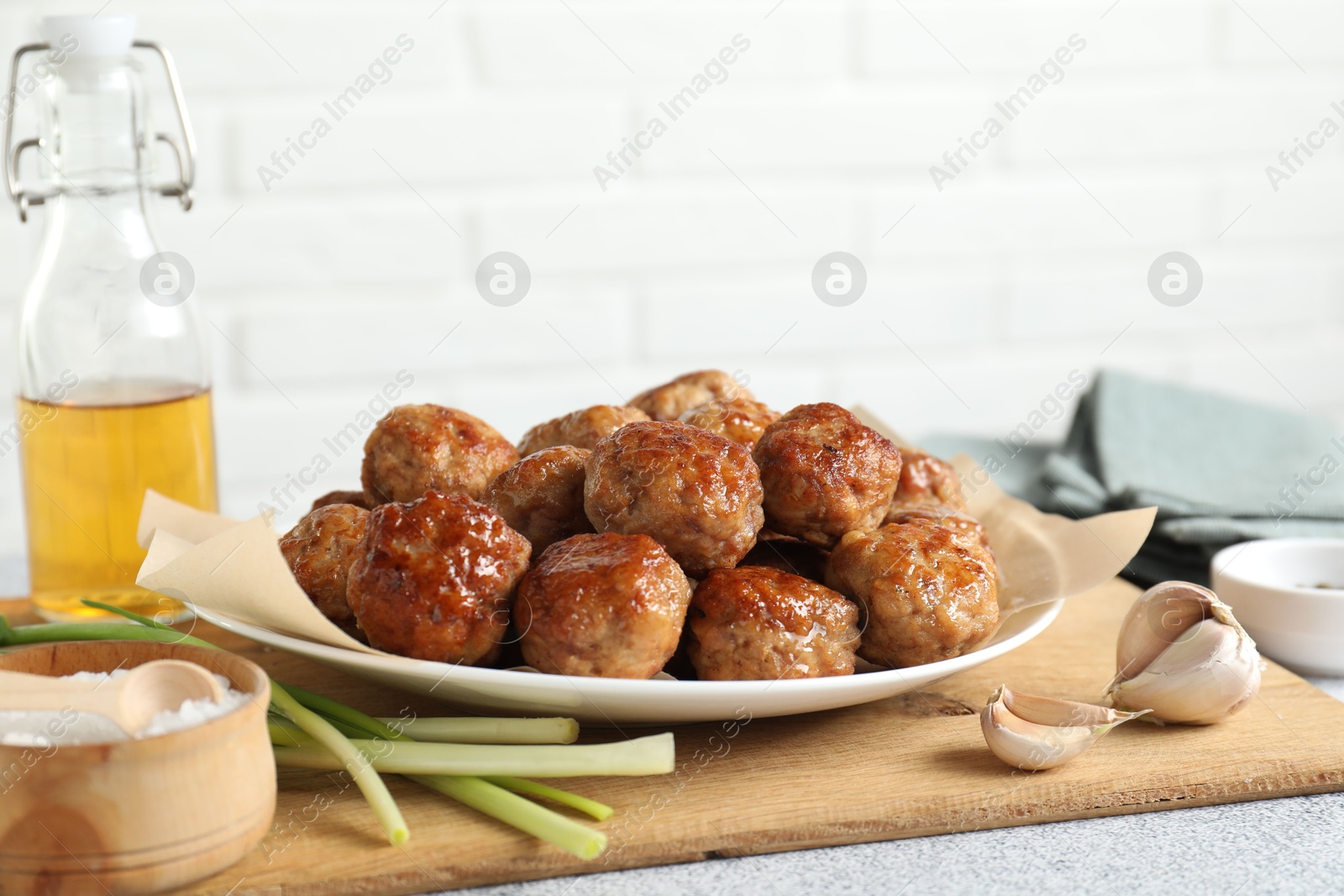 Photo of Many delicious meatballs, green onion, garlic, oil and salt on light textured table, closeup