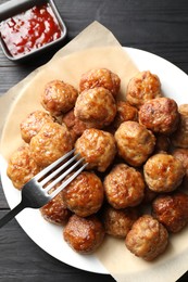 Photo of Many delicious meatballs served with ketchup on dark wooden table, flat lay