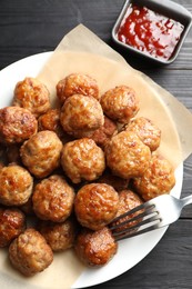 Photo of Many delicious meatballs served with ketchup on dark wooden table, flat lay