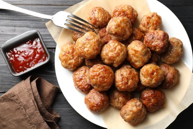 Many delicious meatballs served with ketchup on dark wooden table, flat lay