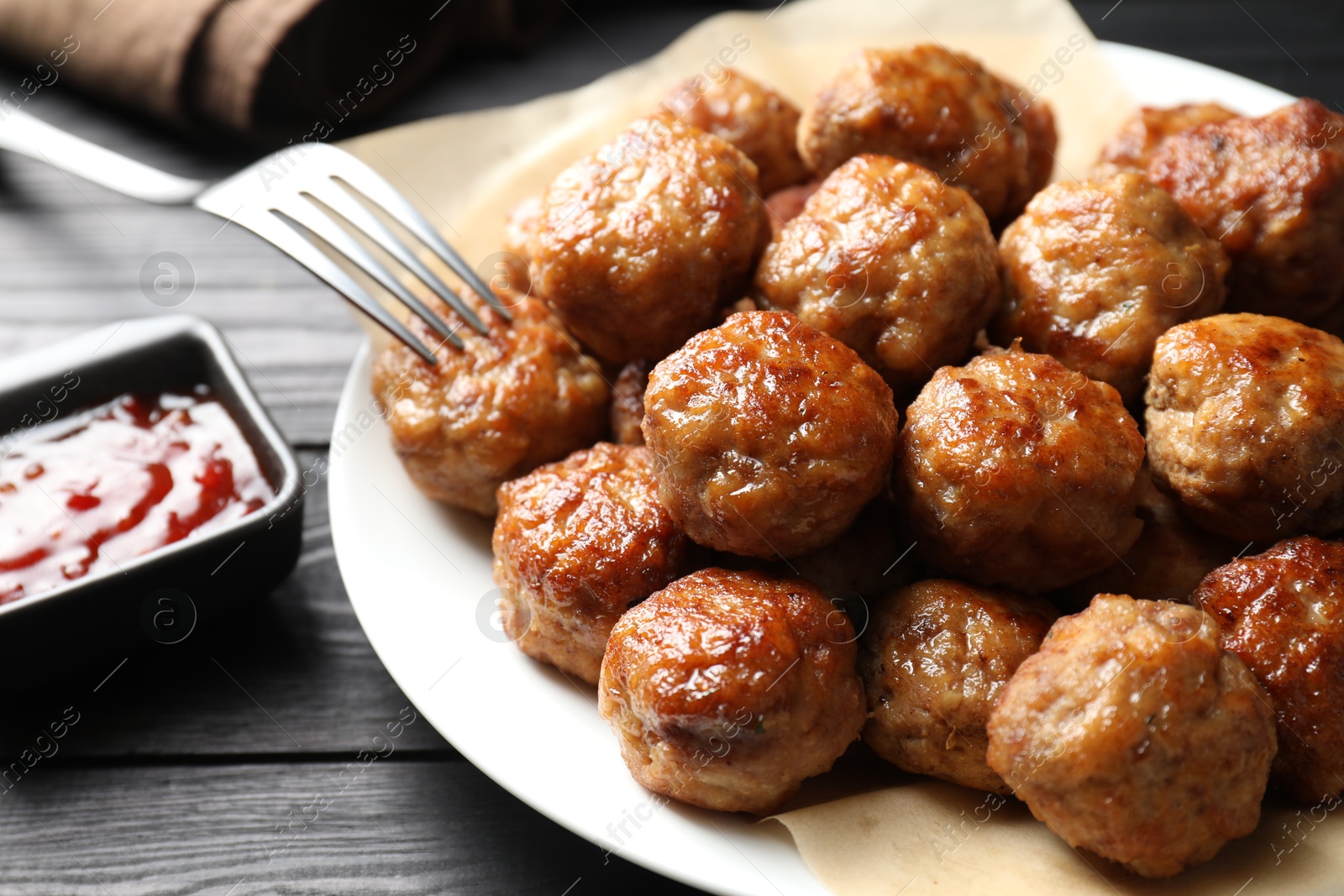 Photo of Many delicious meatballs served with ketchup on dark wooden table, closeup