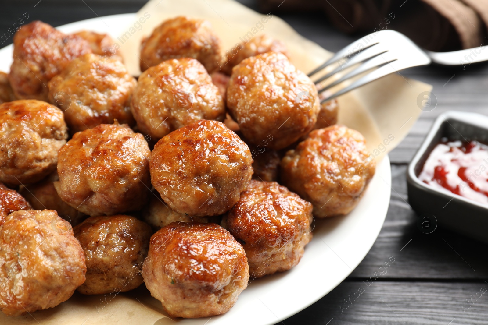 Photo of Many delicious meatballs served with ketchup on dark wooden table, closeup