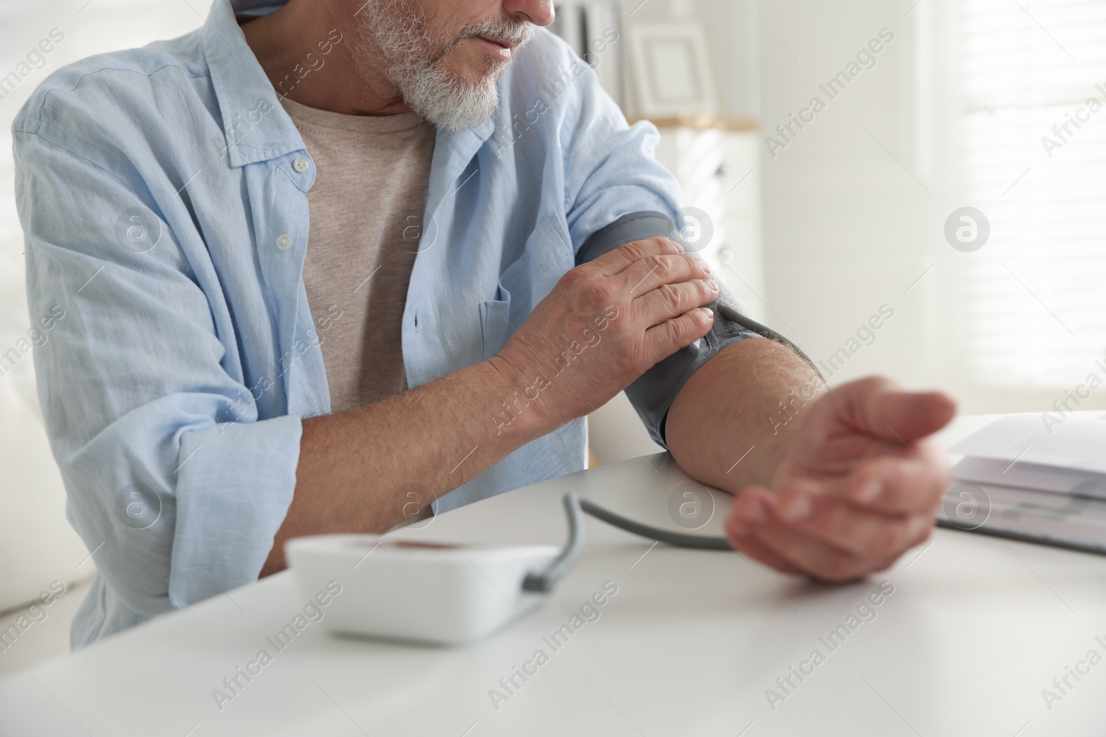 Photo of Senior man measuring blood pressure at table indoors, closeup