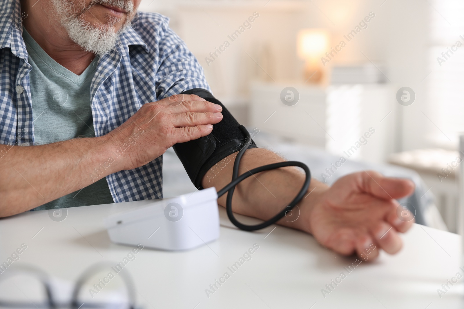 Photo of Senior man measuring blood pressure at table indoors, closeup