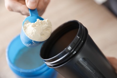 Photo of Making protein cocktail. Man adding powder into shaker at table, closeup