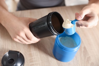 Making protein cocktail. Man adding powder into shaker at wooden table, closeup