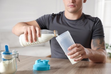 Photo of Making protein cocktail. Man pouring milk into shaker at wooden table, closeup