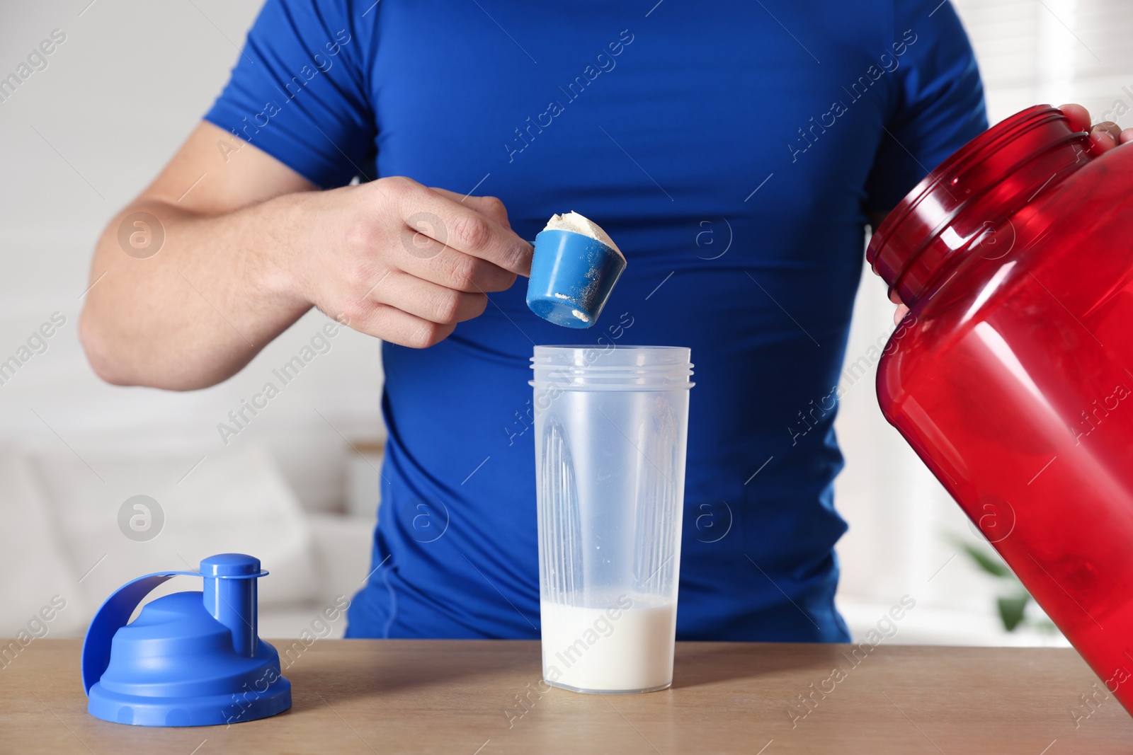 Photo of Making protein cocktail. Man adding powder into shaker at wooden table, closeup