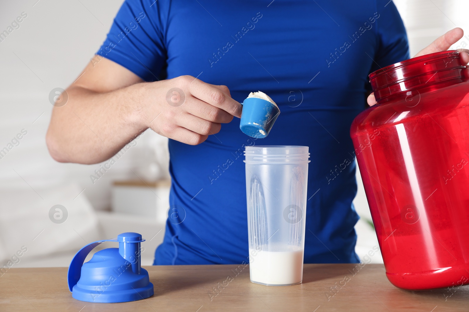 Photo of Making protein cocktail. Man adding powder into shaker at wooden table, closeup