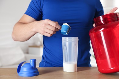 Making protein cocktail. Man adding powder into shaker at wooden table, closeup