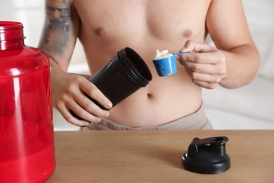 Photo of Making protein cocktail. Man adding powder into shaker at wooden table, closeup