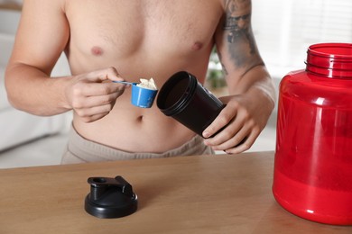 Photo of Making protein cocktail. Man adding powder into shaker at wooden table, closeup