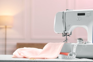 Photo of Sewing machine with threads, measuring tape and fabric on white table in workshop, space for text