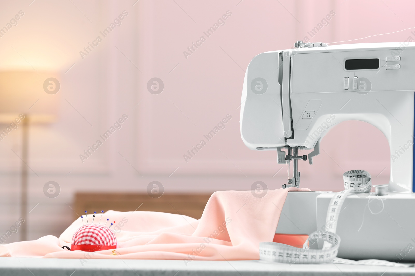 Photo of Sewing machine with fabric and other supplies on white table in workshop, space for text