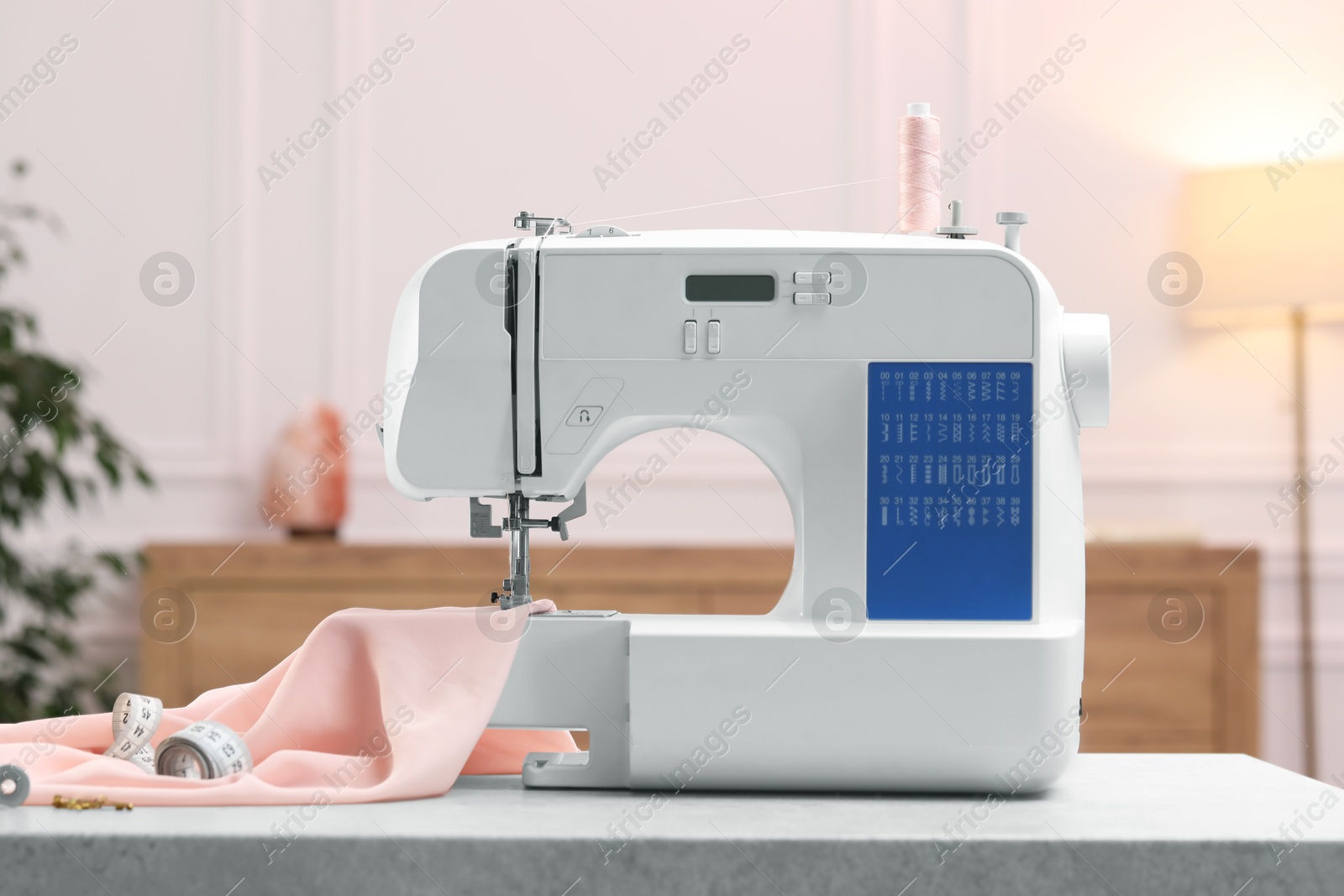 Photo of Sewing machine with threads, measuring tape and fabric on white table in workshop