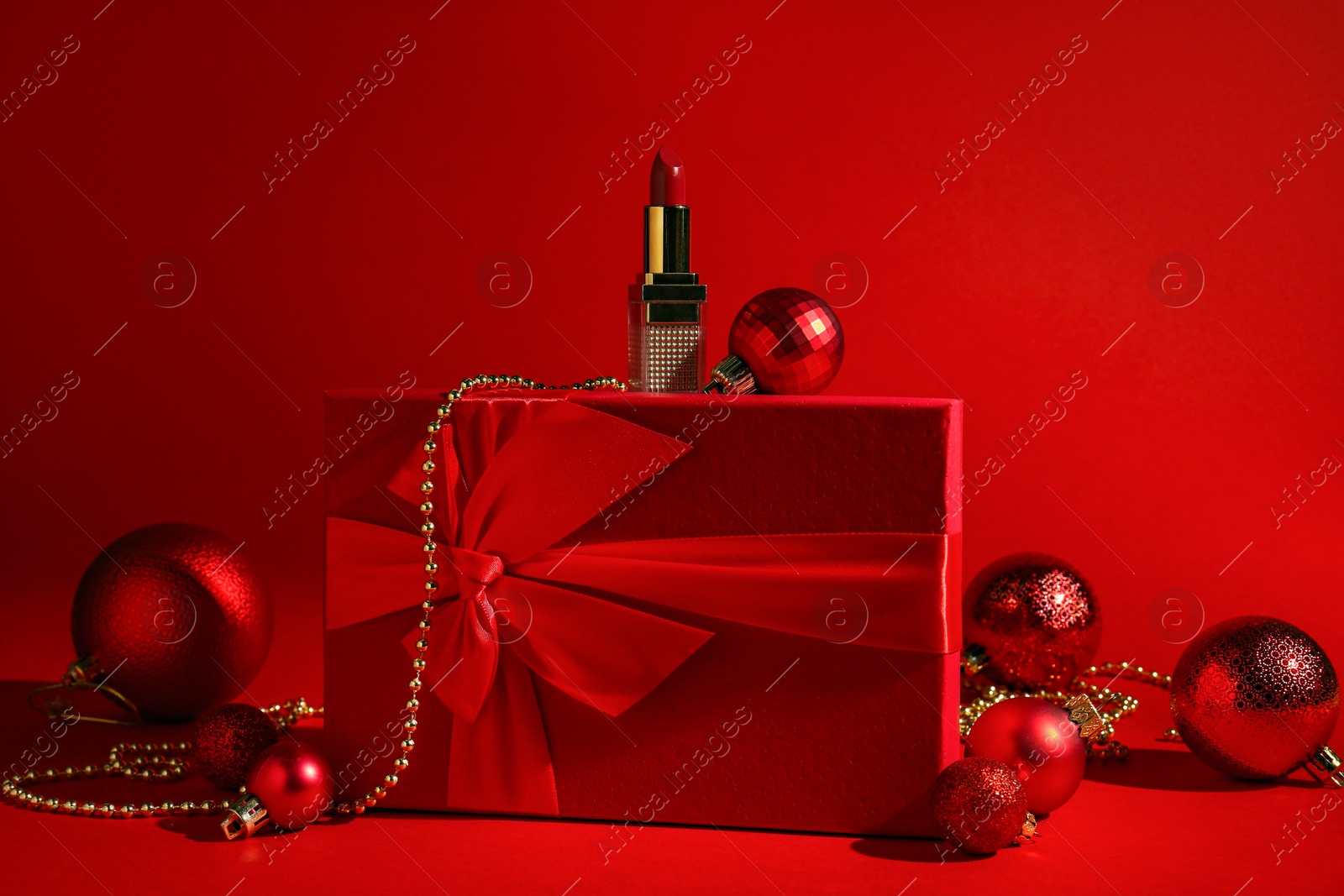 Photo of Christmas present. Lipstick, gift box and festive decor on red background