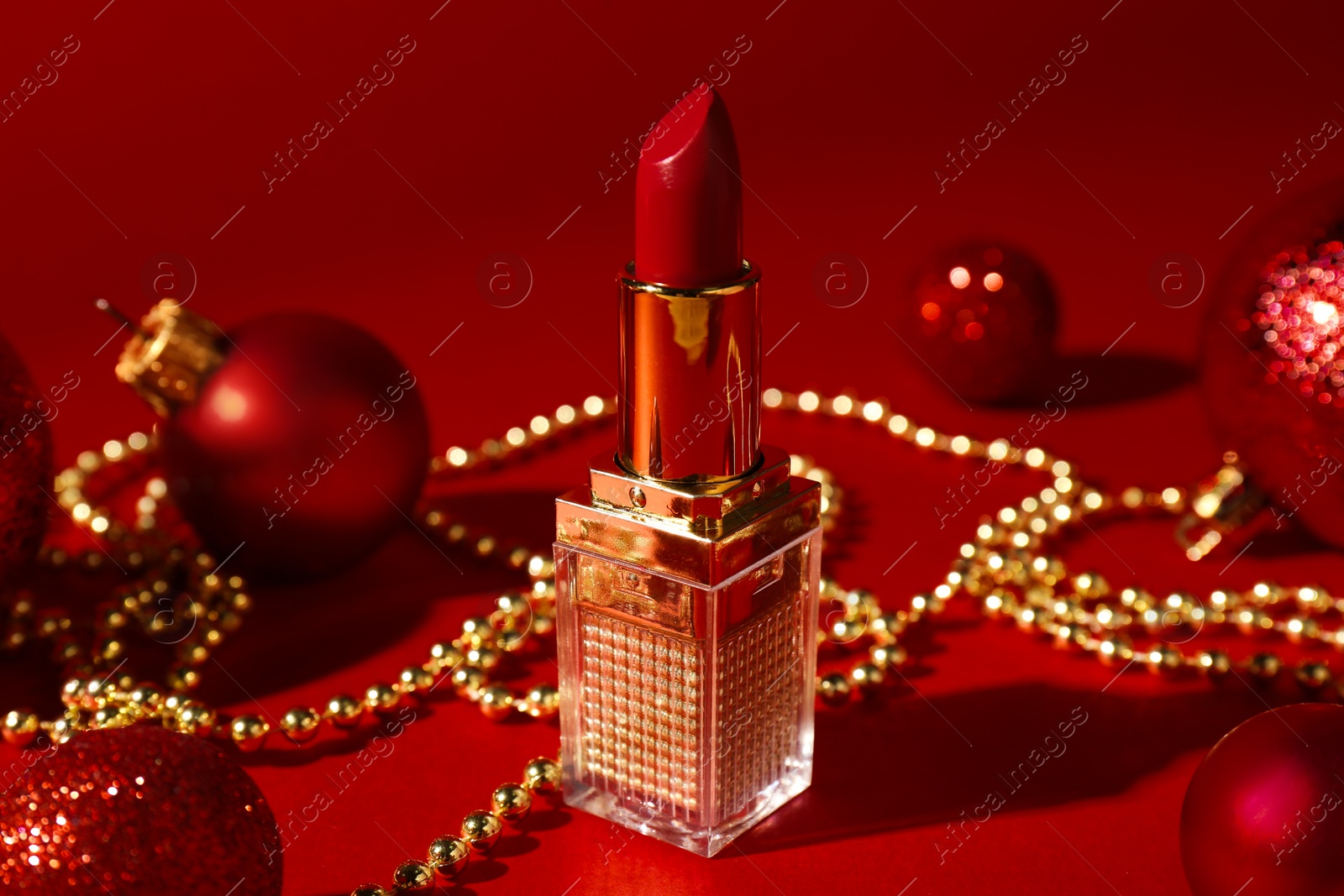 Photo of Christmas gift. Lipstick and festive decor on red background, closeup