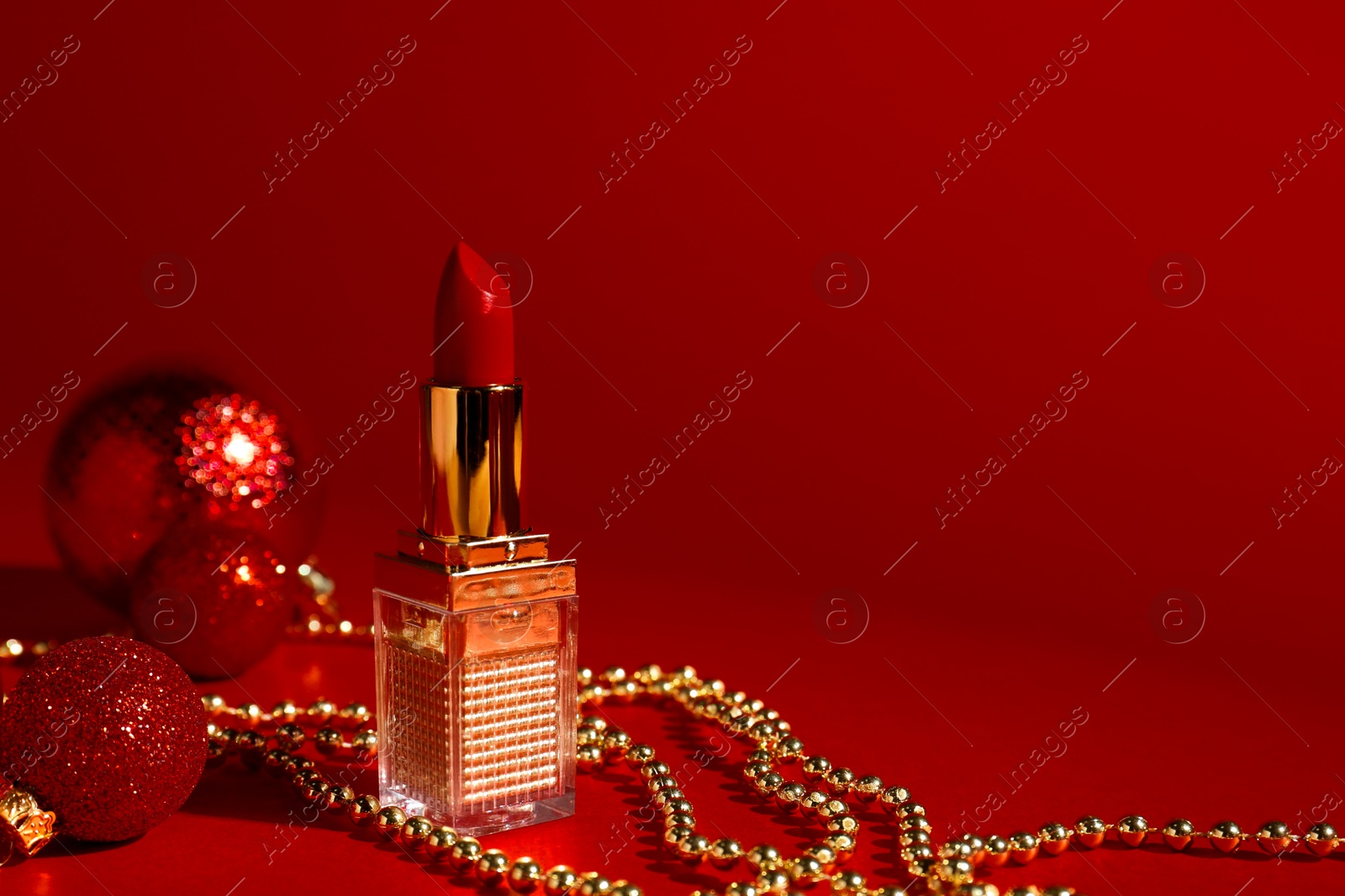 Photo of Christmas gift. Lipstick and festive decor on red background. Space for text