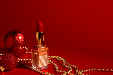 Photo of Christmas gift. Lipstick and festive decor on red background. Space for text