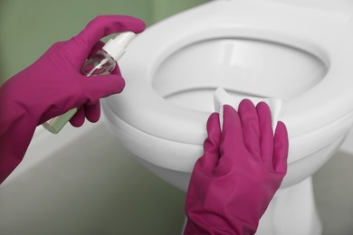 Photo of Woman disinfecting toilet seat in restroom, closeup